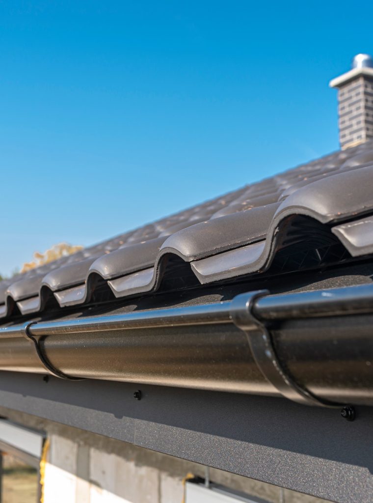 A metal, black gutter on a roof covered with ceramic tiles. Close up shot.